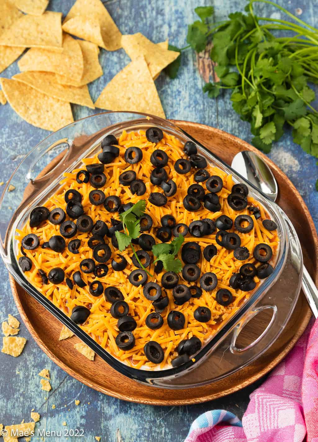 An overhead shot of a pan of Mexican bean dip next to chips, cilantro, and a towel.