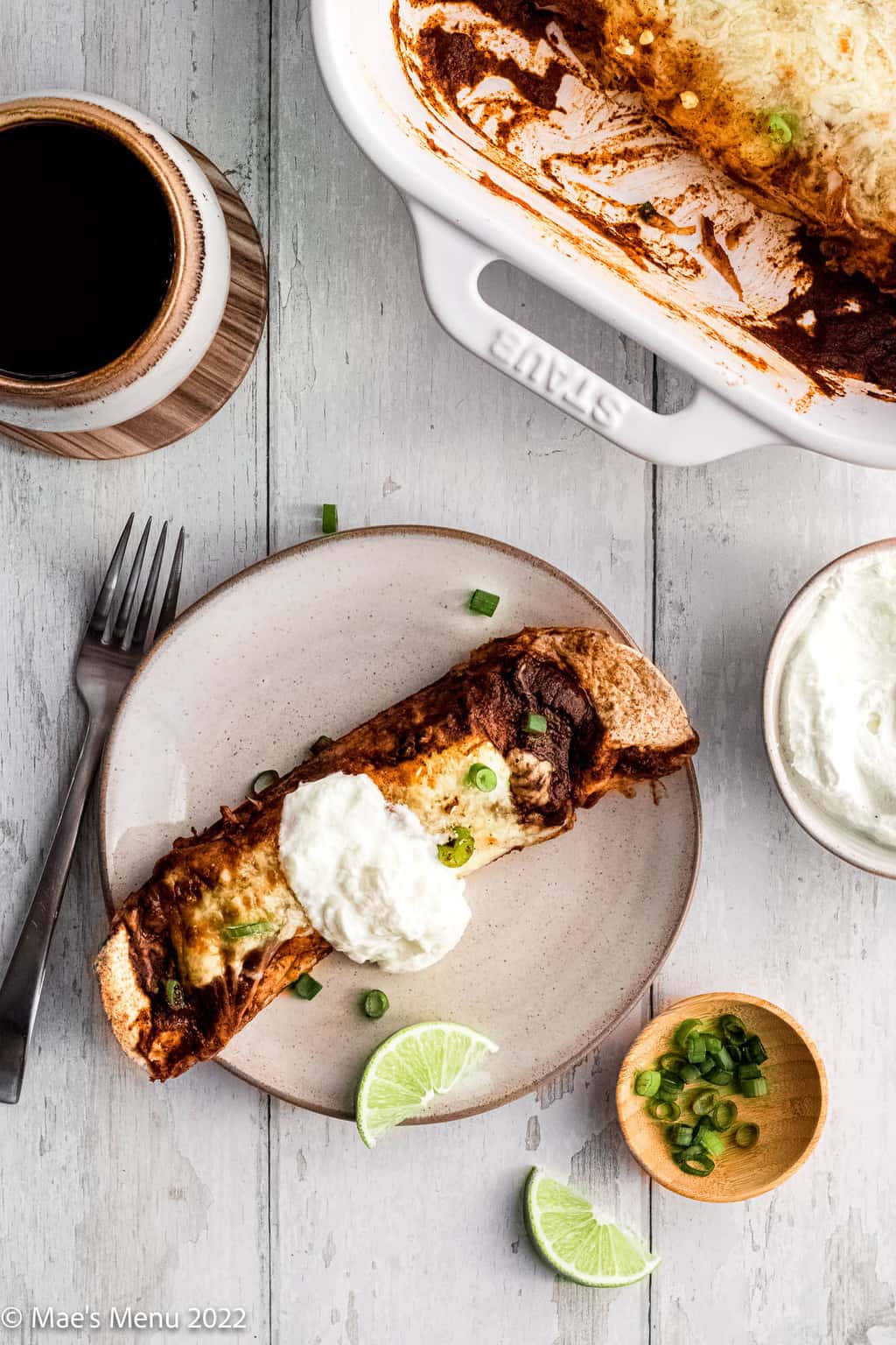 A breakfast enchilada on a plate with sour cream and green onions on it.