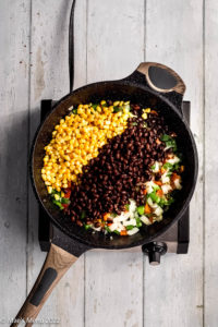 An overhead shot of a pan of peppers, corn, and beans in a skillet.