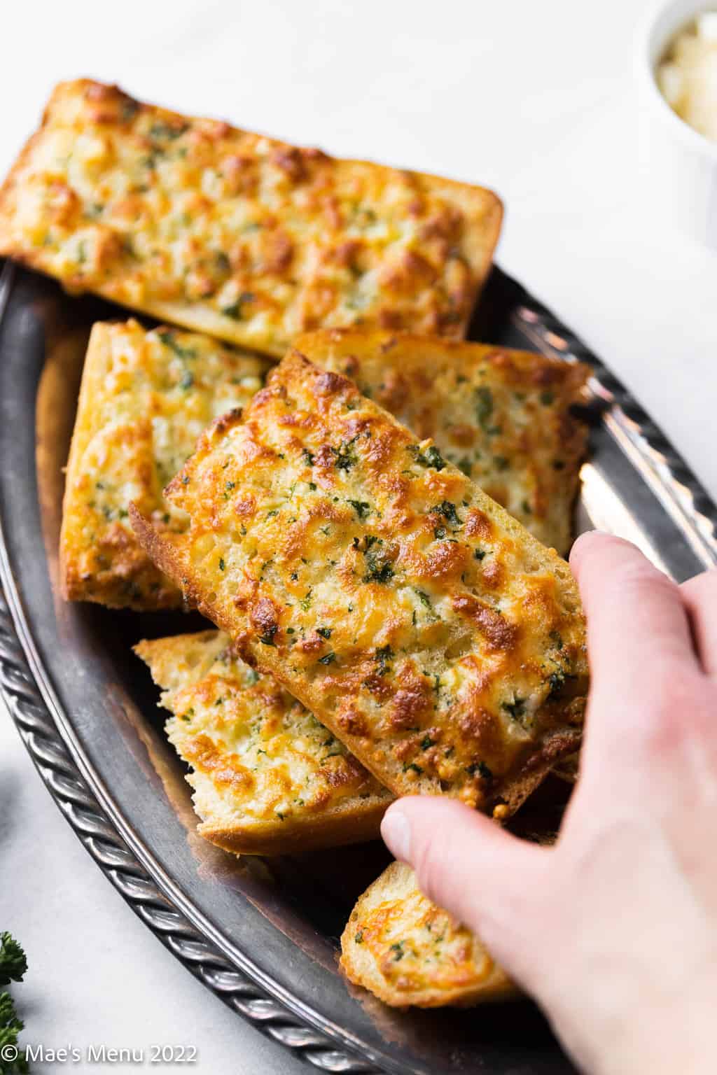 A hand grabbing a piece of garlic bread from a tray.