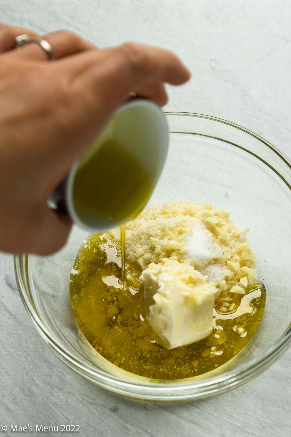 Pouring olive oil into a small boil of butter, cheese, and garlic.