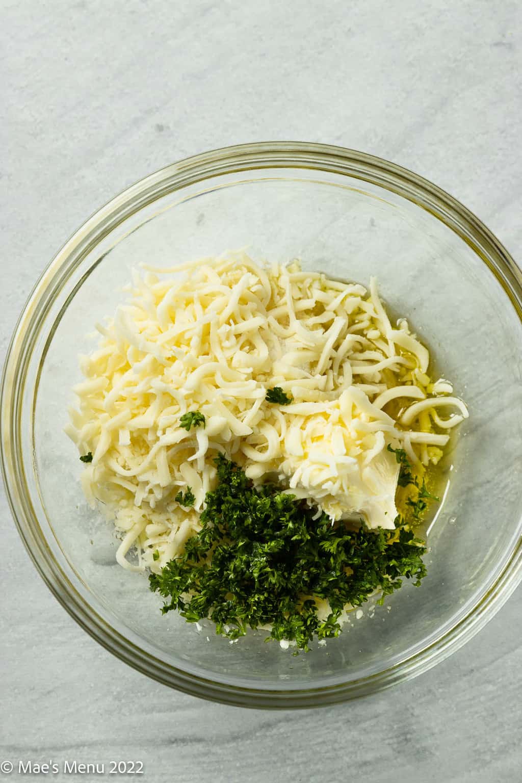 An overhead of a small mixing bowl of cheese, parsley, butter, and oil.