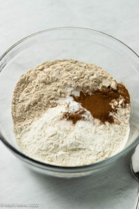 A clear mixing bowl of flours, cinnamon, and baking powder.