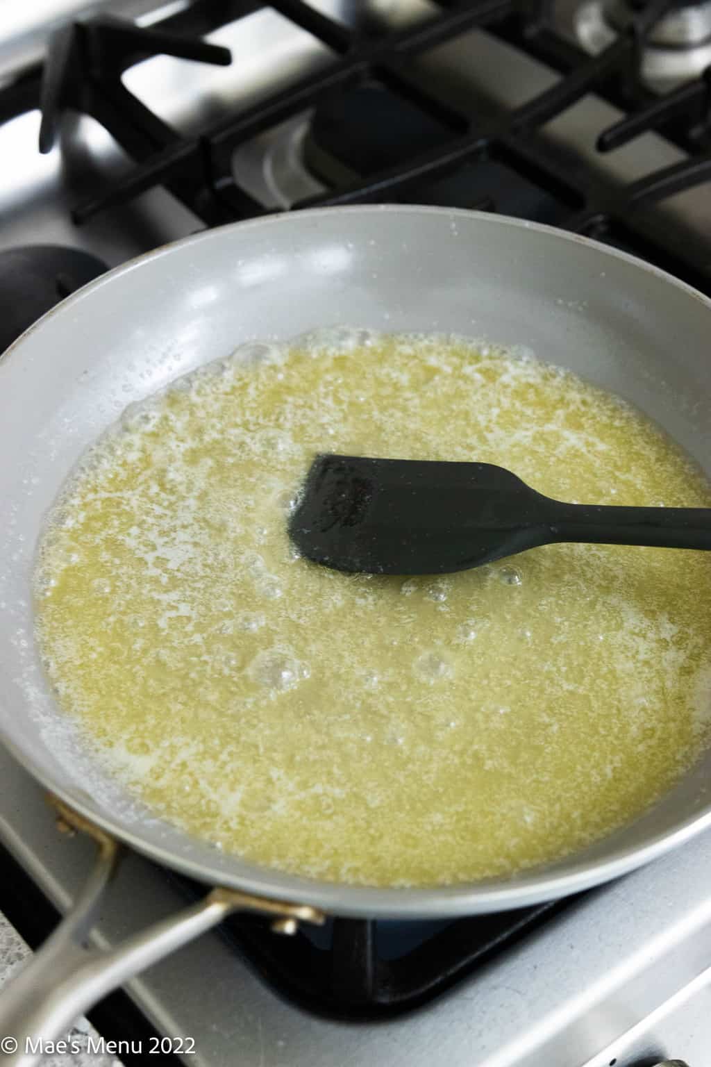 An overhead shot of grey pan with foaming butter and a silicone spatula.