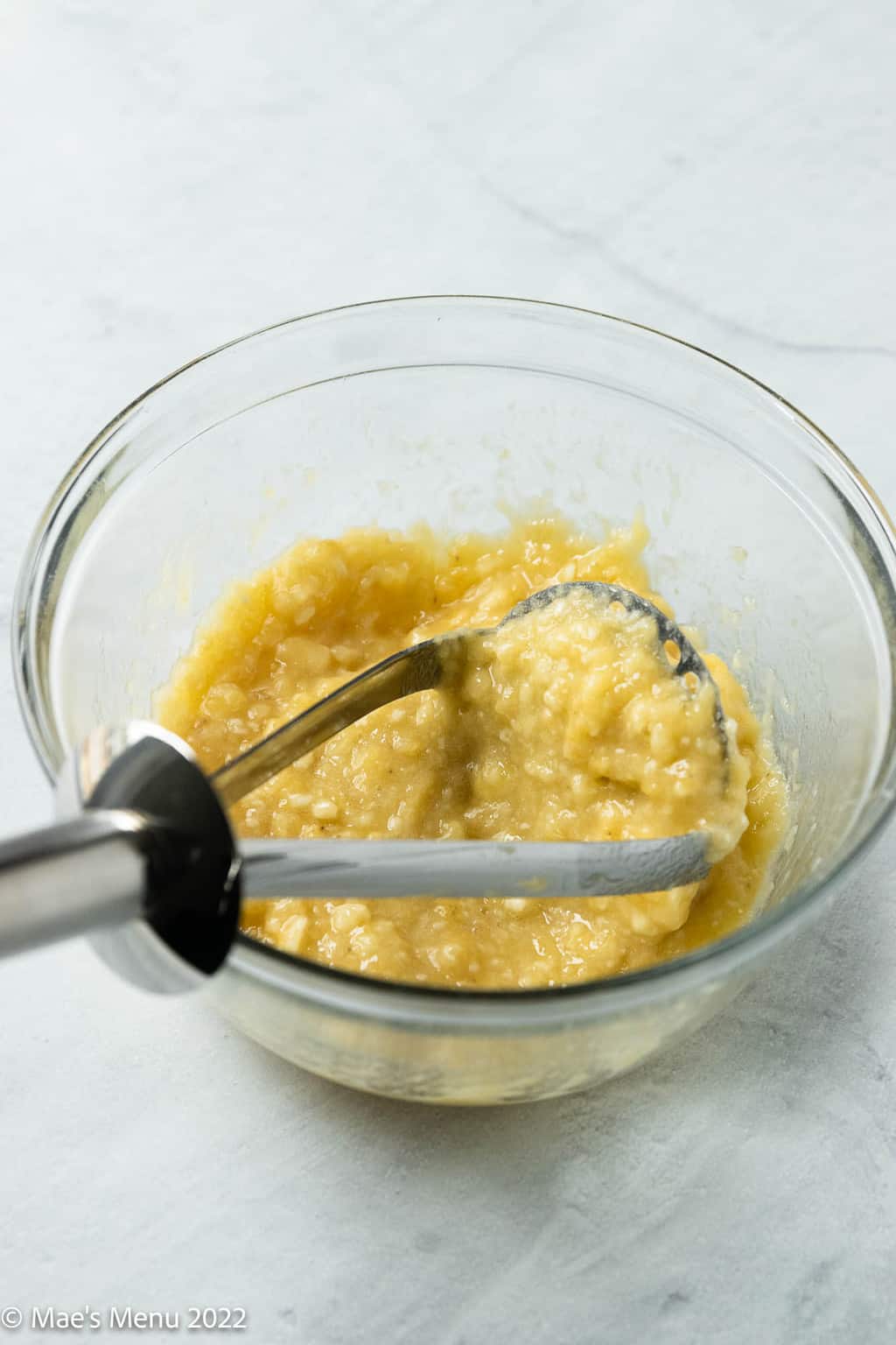A bowl of mashed bananas with a potato masher.