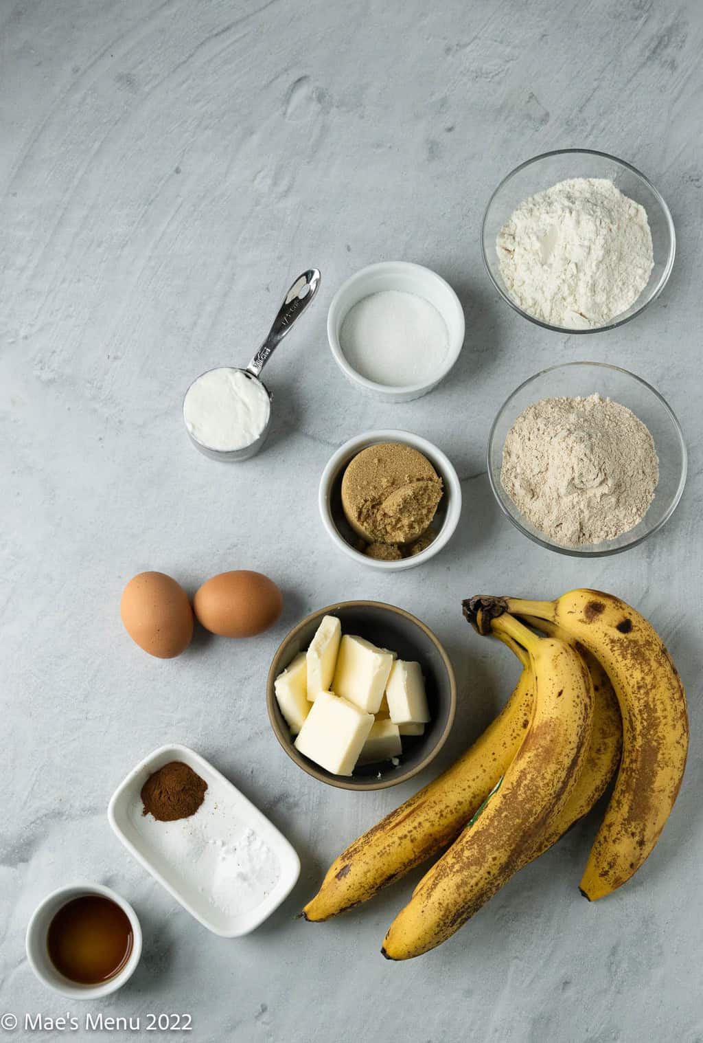 All of the ingredients for brown butter banana bread: flours, sugar, brown sugar, greek yogurt, eggs, butter, overripe bananas, vanilla, cinnamon, and seasonings.