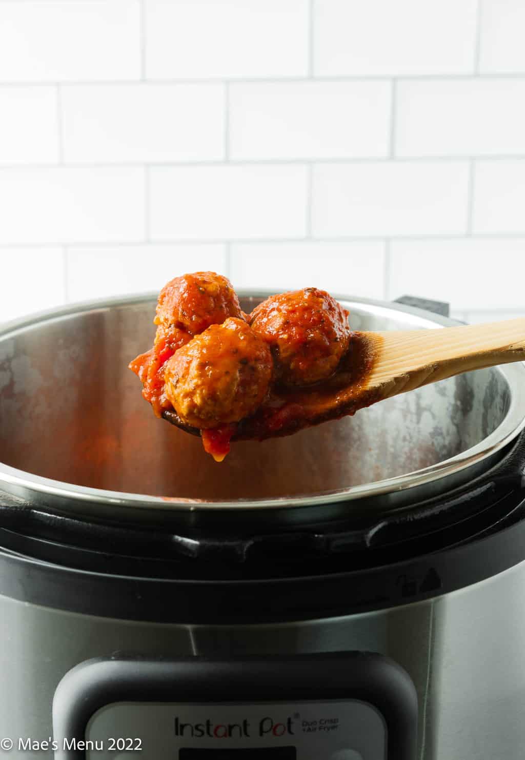 A side shot of a wooden spoon scooping meatballs out of the Instant Pot.