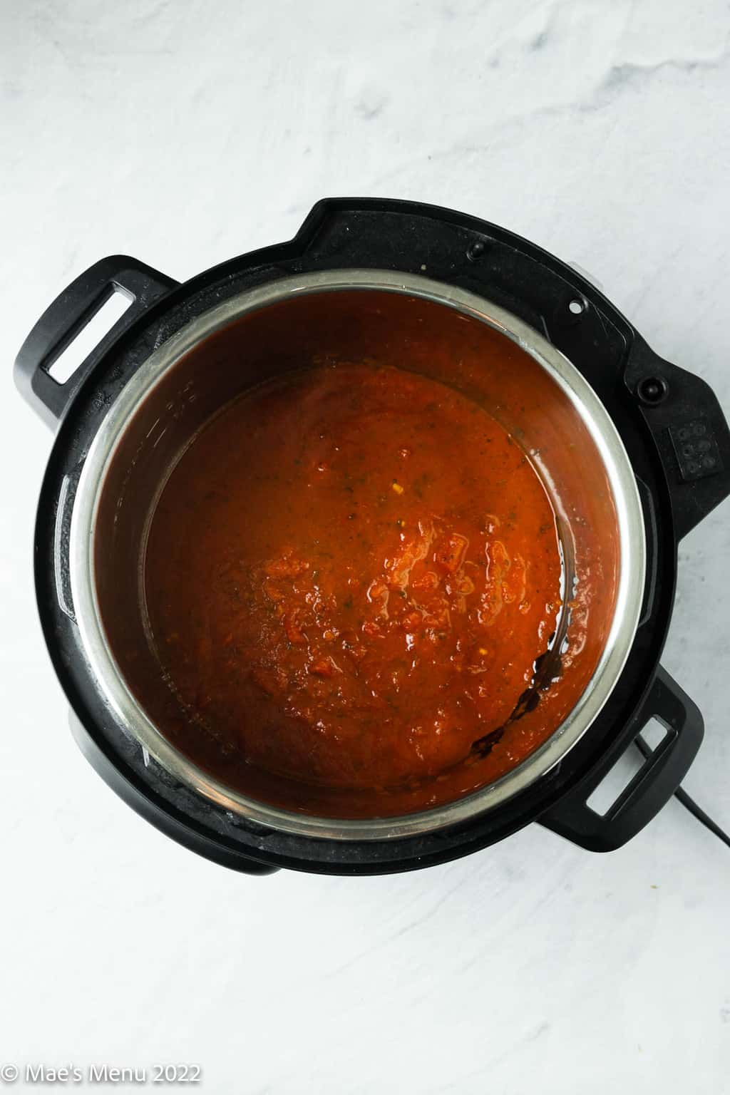 An overhead shot of an Instant pot with tomato sauce and olive oil.