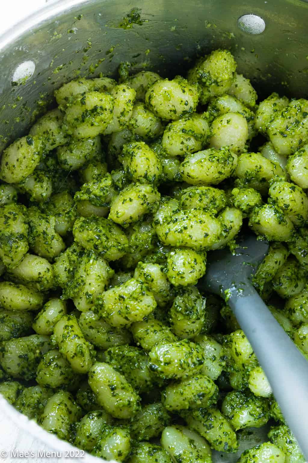 An up-close overhead shot of a large pot with pesto gnocchi and a spatula.