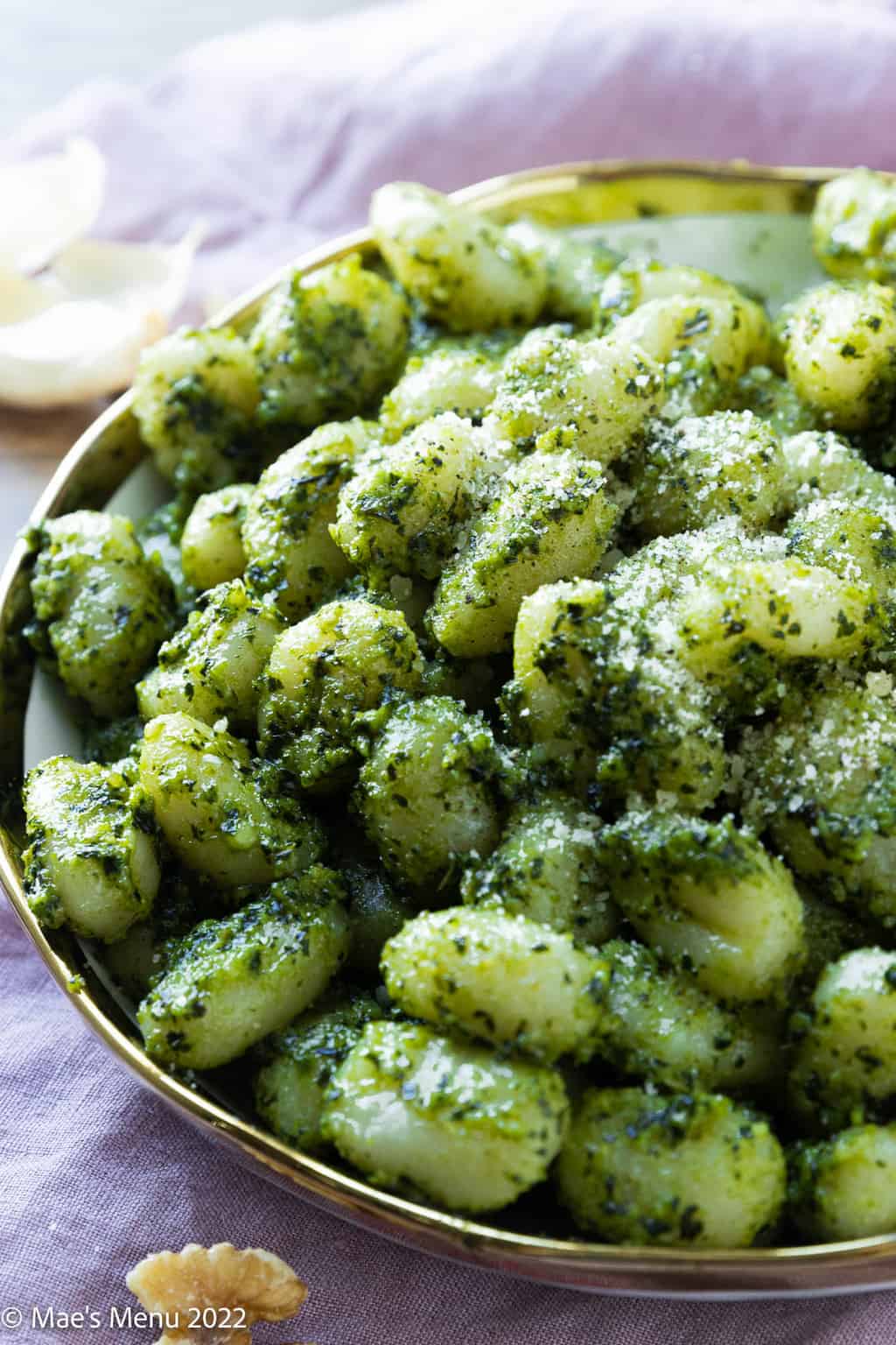 An up-close side shot of a bowl of pesto gnocchi sprinkled with parmesan cheese.