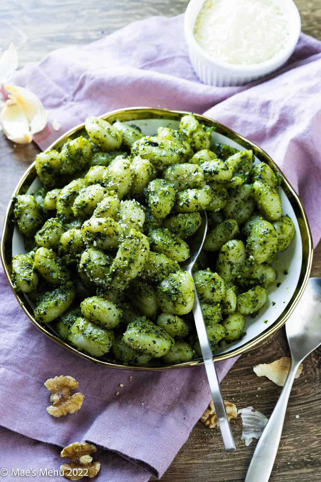 An angled overhead shot of a white and gold bowl of pesto gnocchi with a spoon in it.