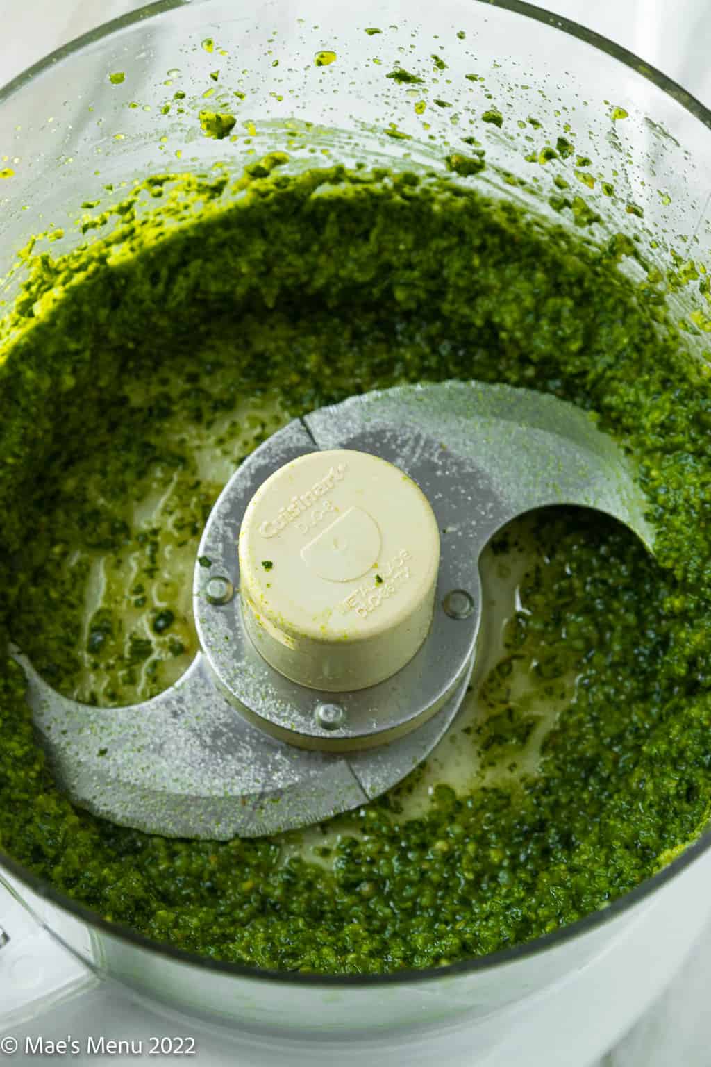 An up-close shot of green pesto in the bowl of a food processor.