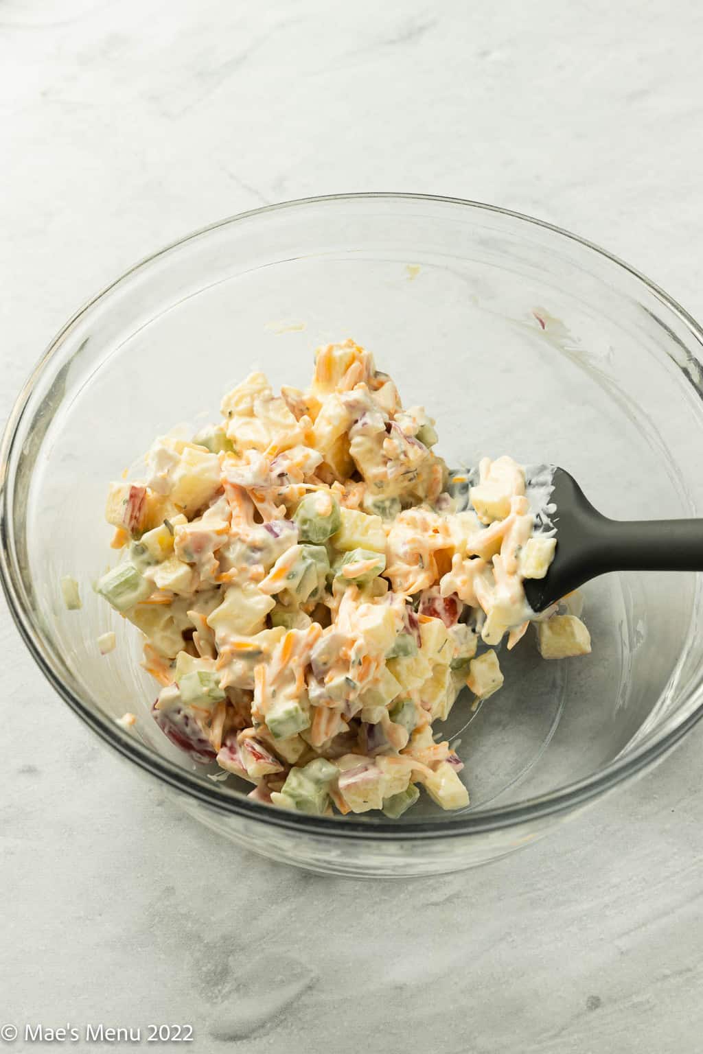 A glass mixing bowl with chicken, celery, and apples tossed in the dressing.