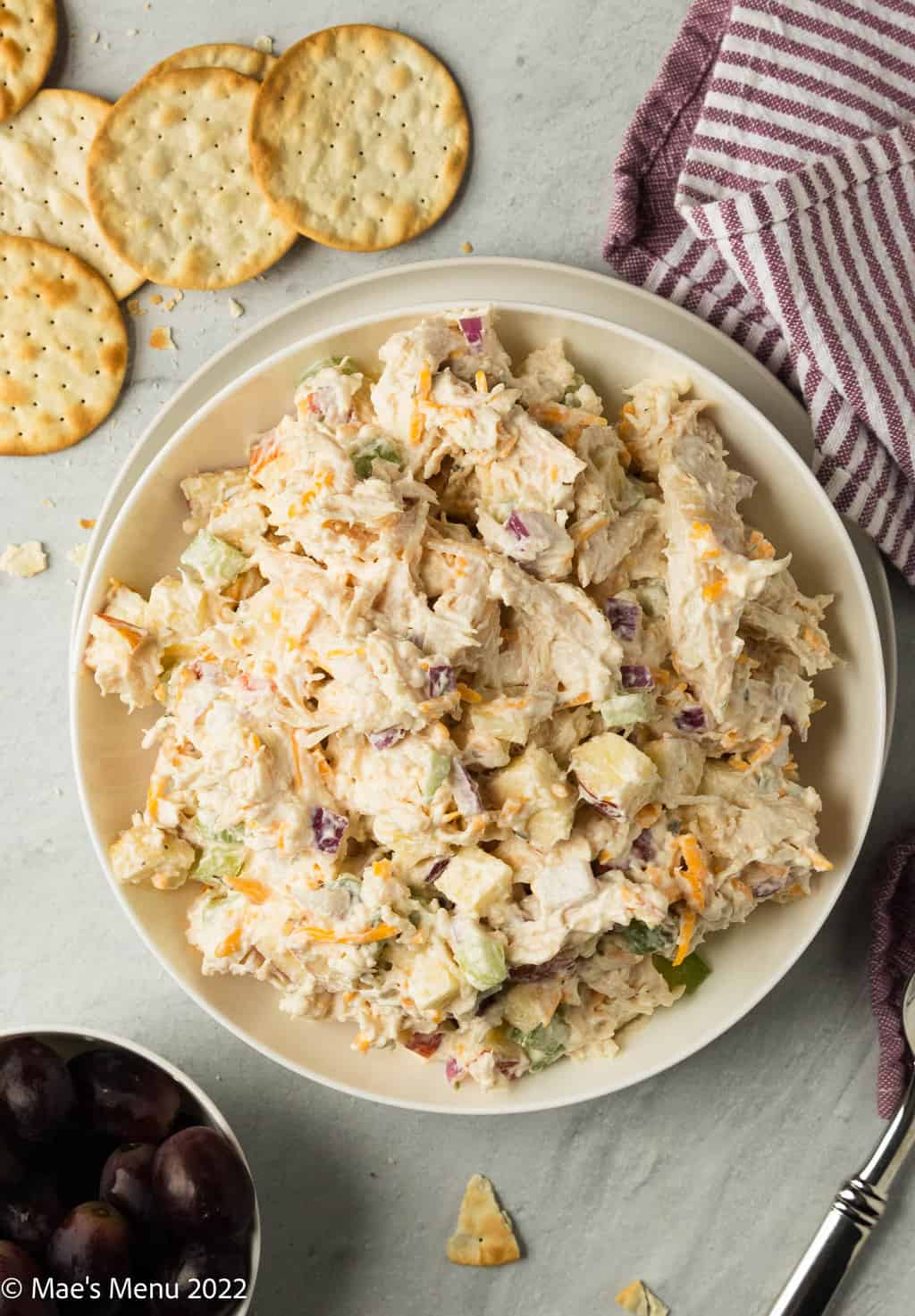 An overhead shot of a bowl of rotisserie chicken salad surrounded by crackers and grapes.