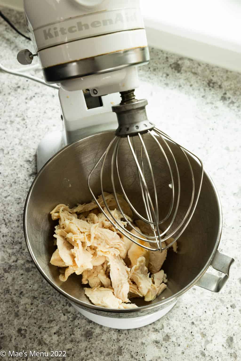 An overhead shot of a stand mixer of chicken in it.