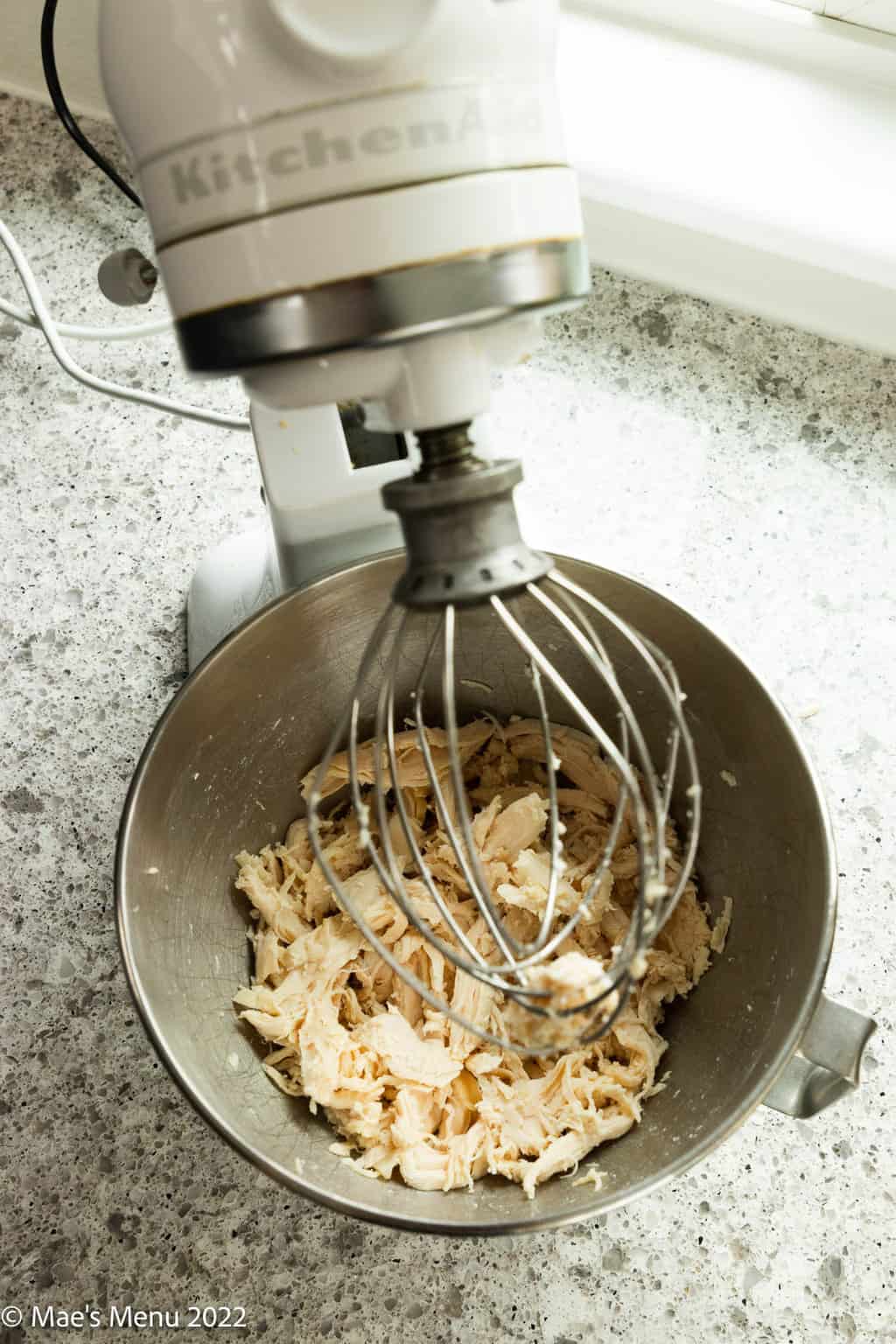 An overhead shot of a mixing bowl with shredded chicken in it.