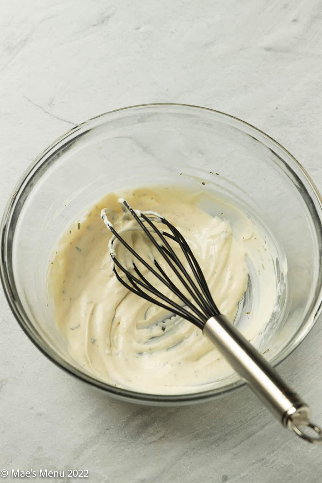 A glass mixing bowl with a whisk and dressing.