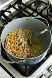 A stockpot on a gas oven range with ground turkey and vegetables.
