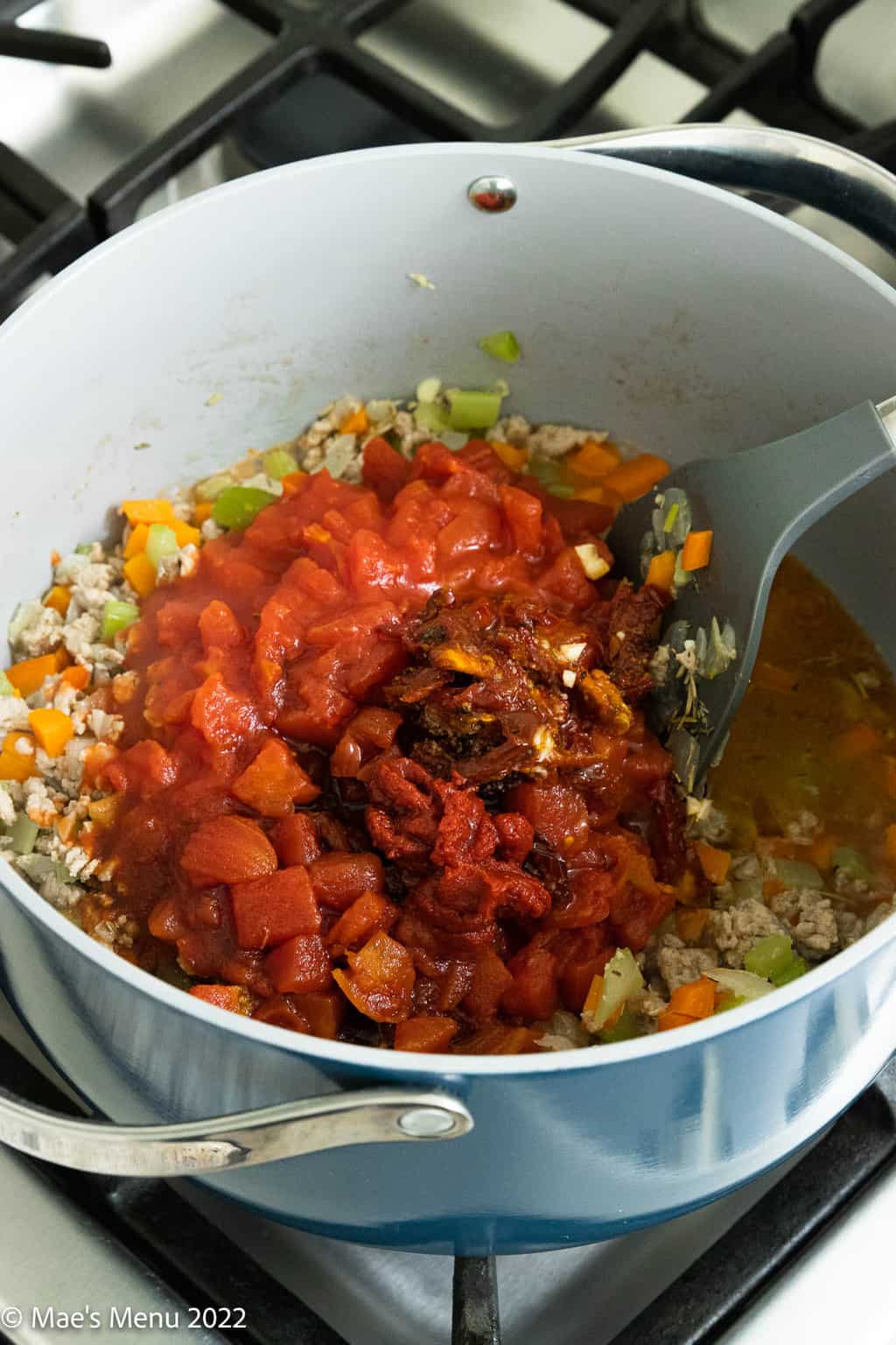 A stock pot with ground turkey, vegetables, canned tomatoes, sundried tomatoes, and tomato paste.