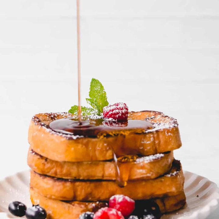 A stack of brioche french toast with maple syrup drizzling on top.