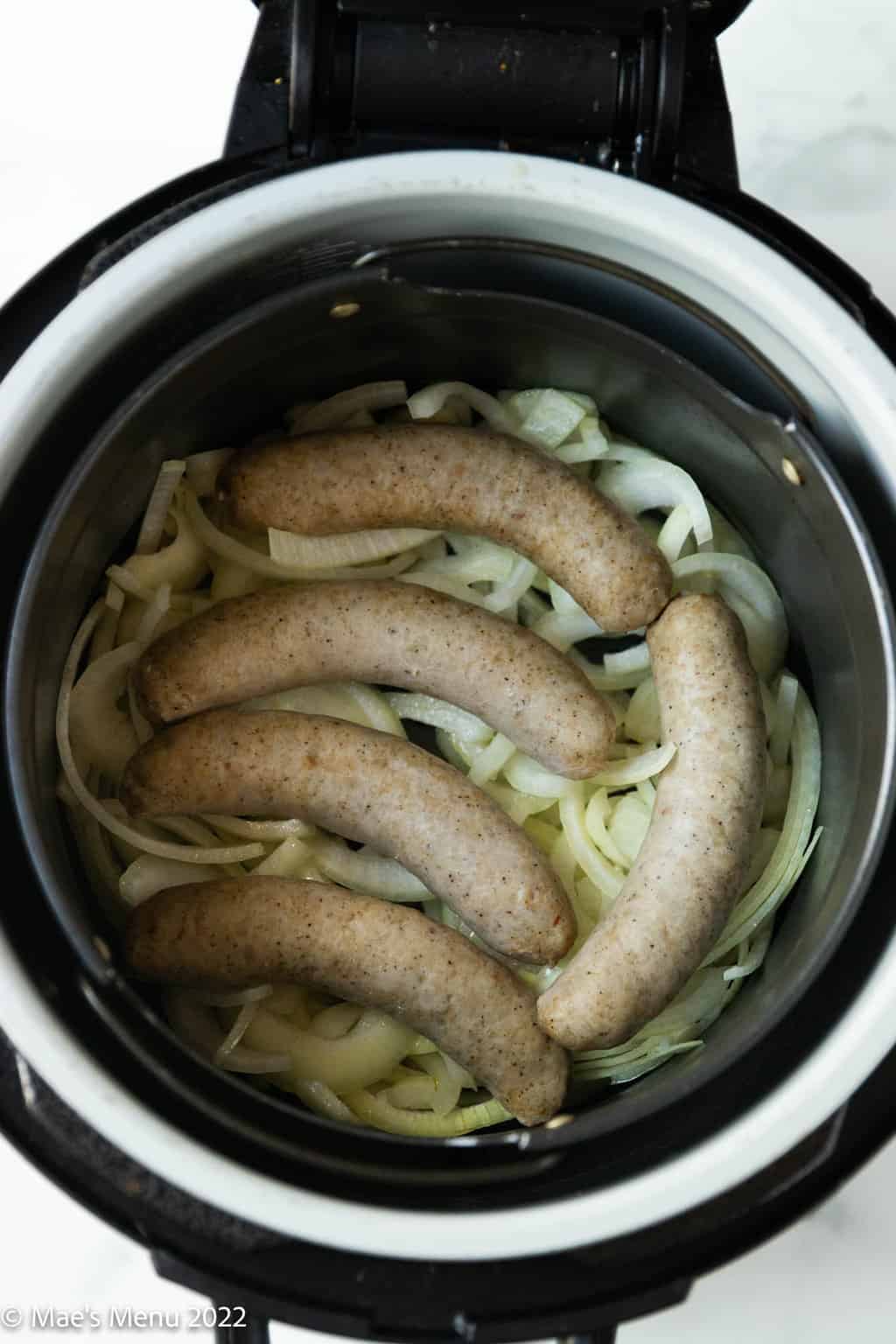 An over head shot of an air fryer with onions and brats.