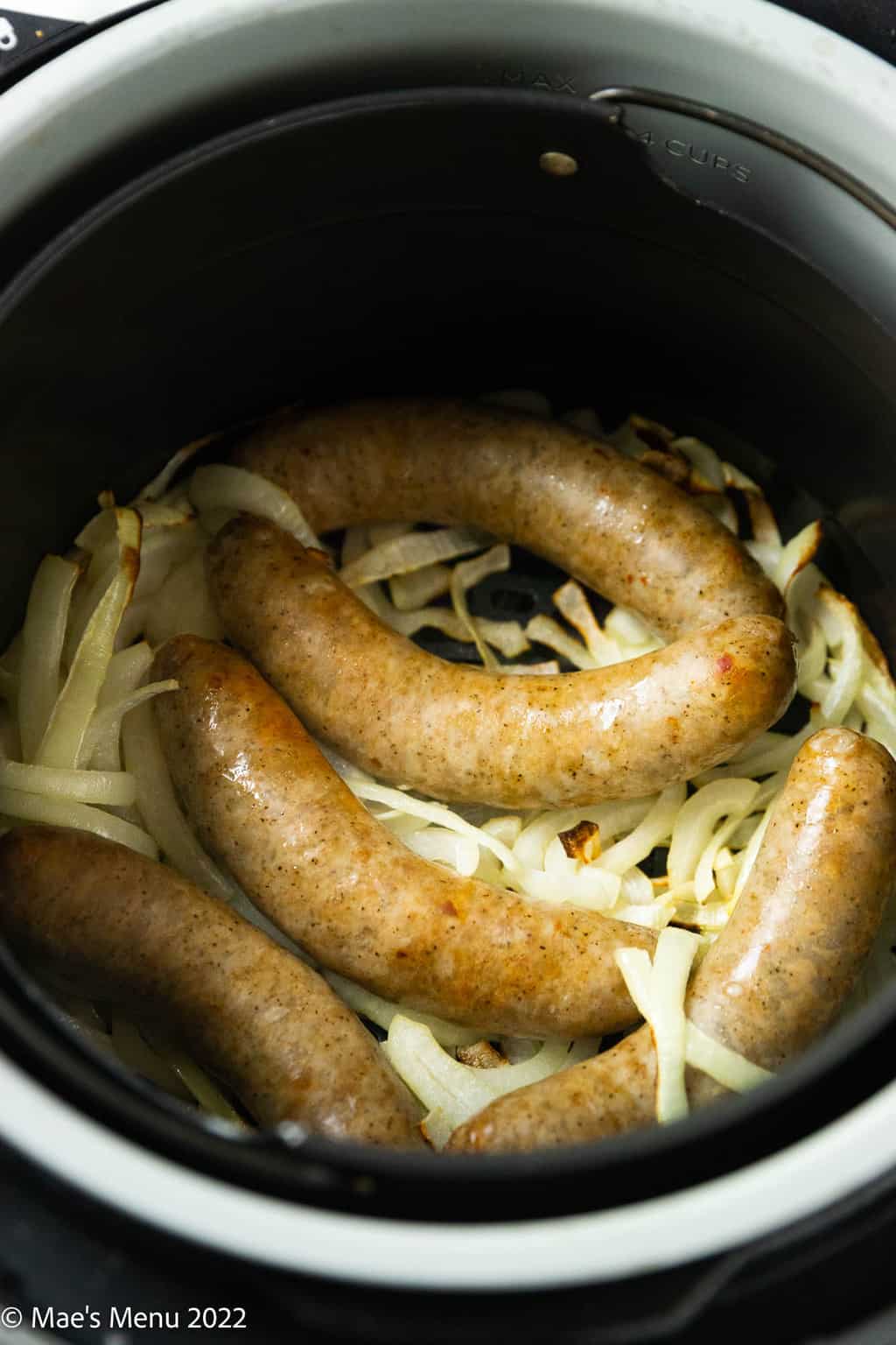 An angled shot of an air fryer with onions and fried brats.