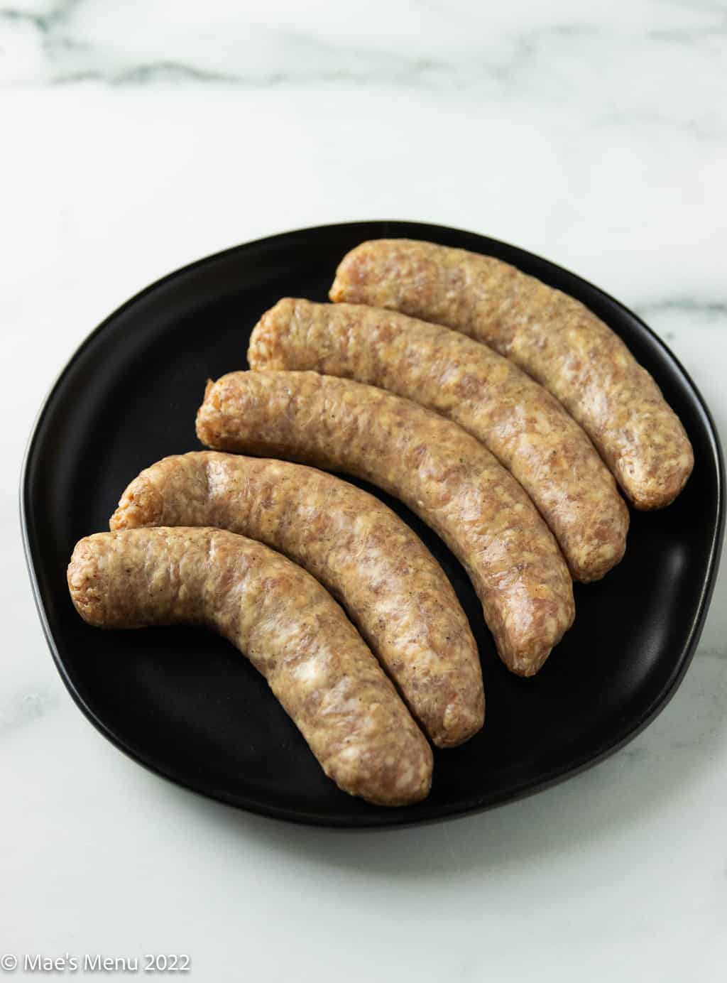 A black plate of uncooked brats.