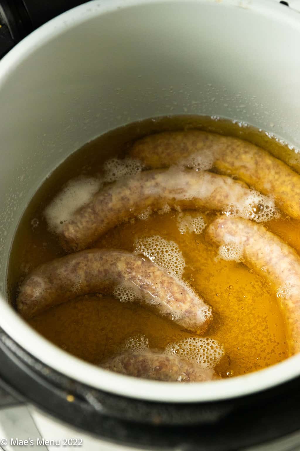 A pressure cooker with beer and brats in it.
