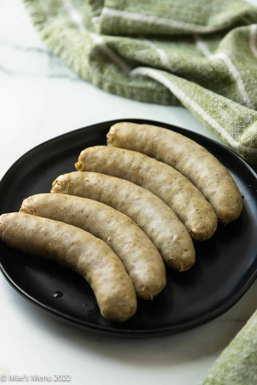 Parboiled brats on a black plate.