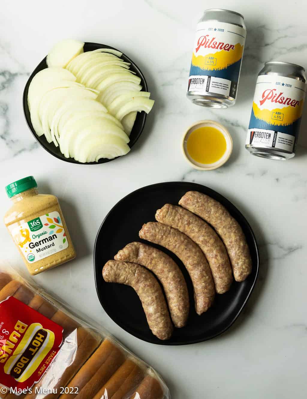 All of the ingredients for air fryer brats: beer, olive oil, onions, mustard, brats, and hot dog buns.