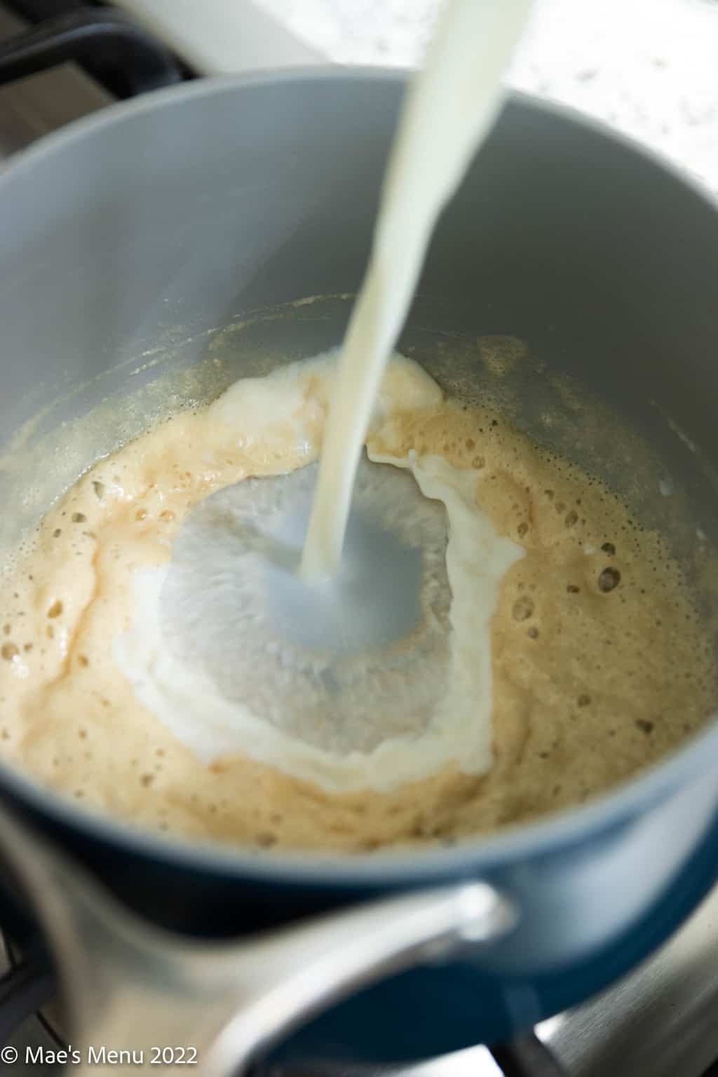 Pouring milk into a saucepan of roux.