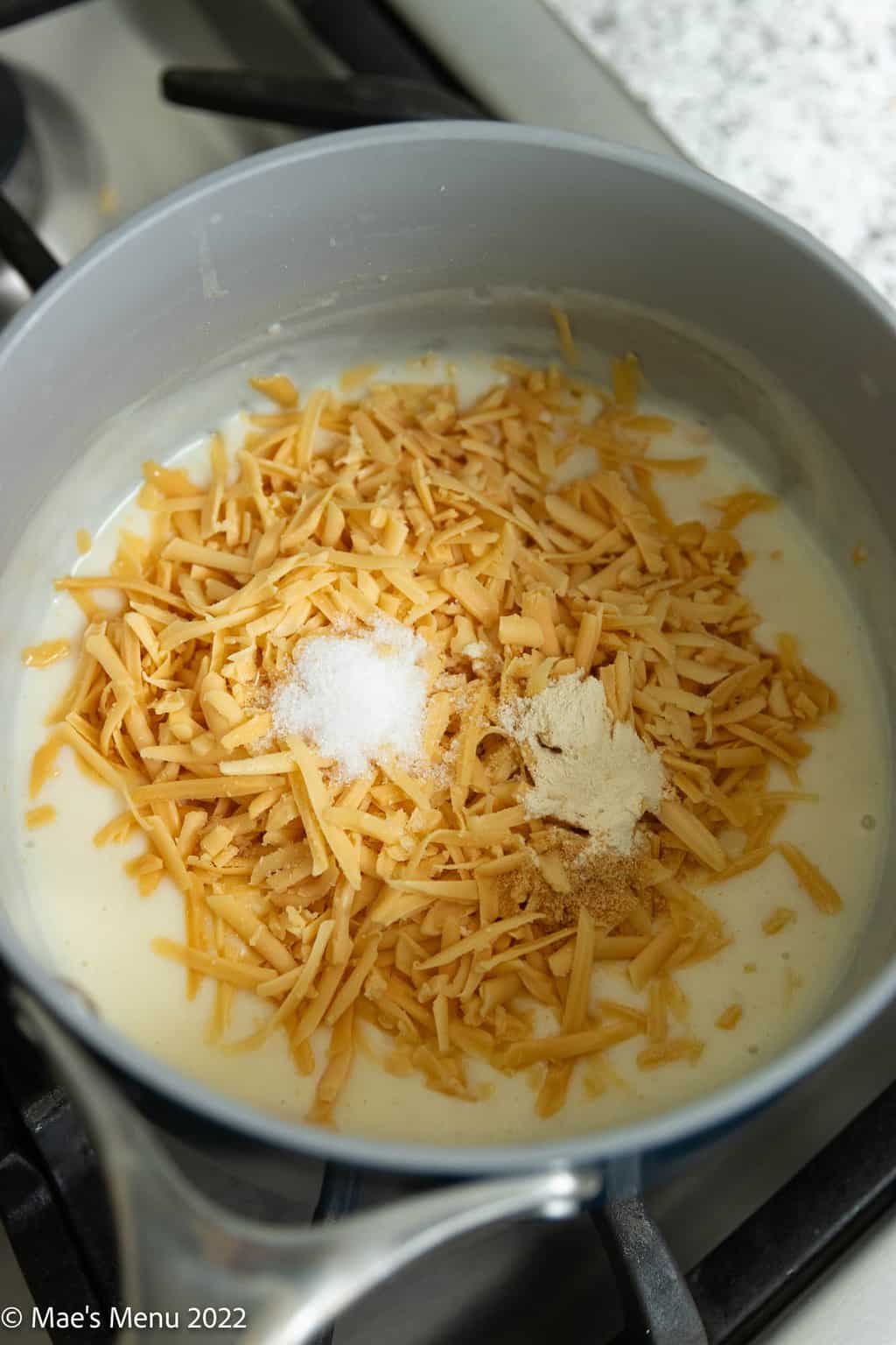 A saucepan with roux, shredded cheese, and seasonings.