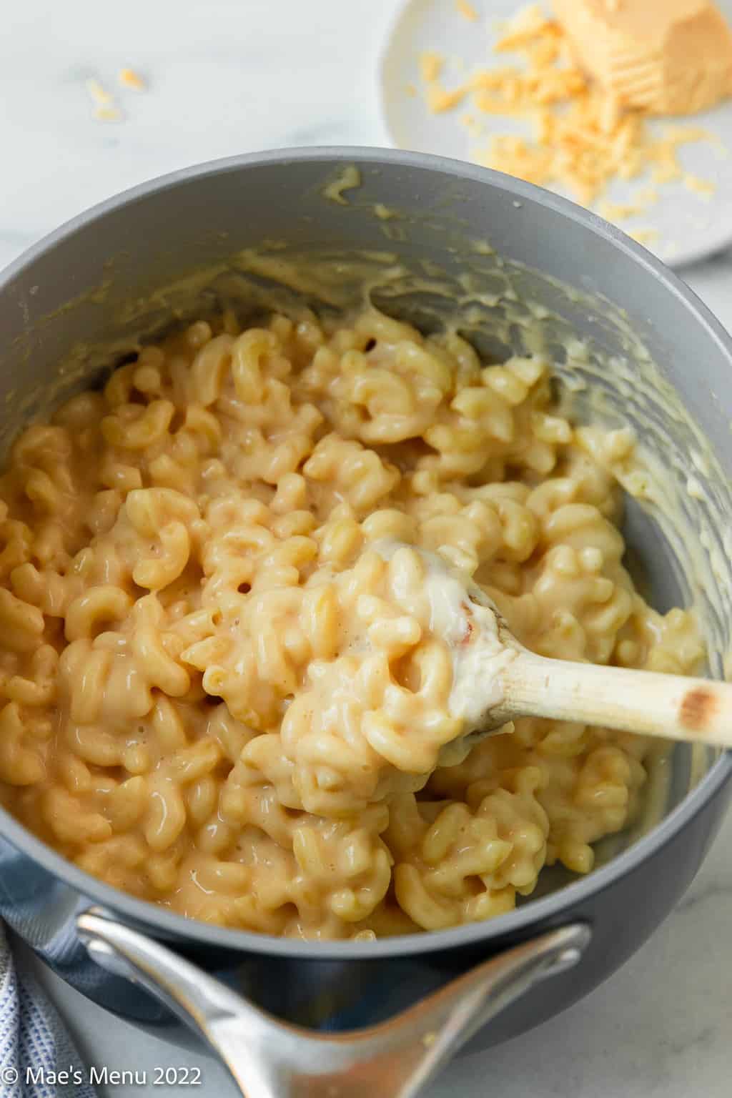 A saucepan of smoked gouda mac and cheese with a wooden spoon.