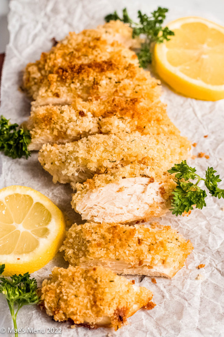 An up-close shot of a sliced panko chicken breast with parsley and lemon.