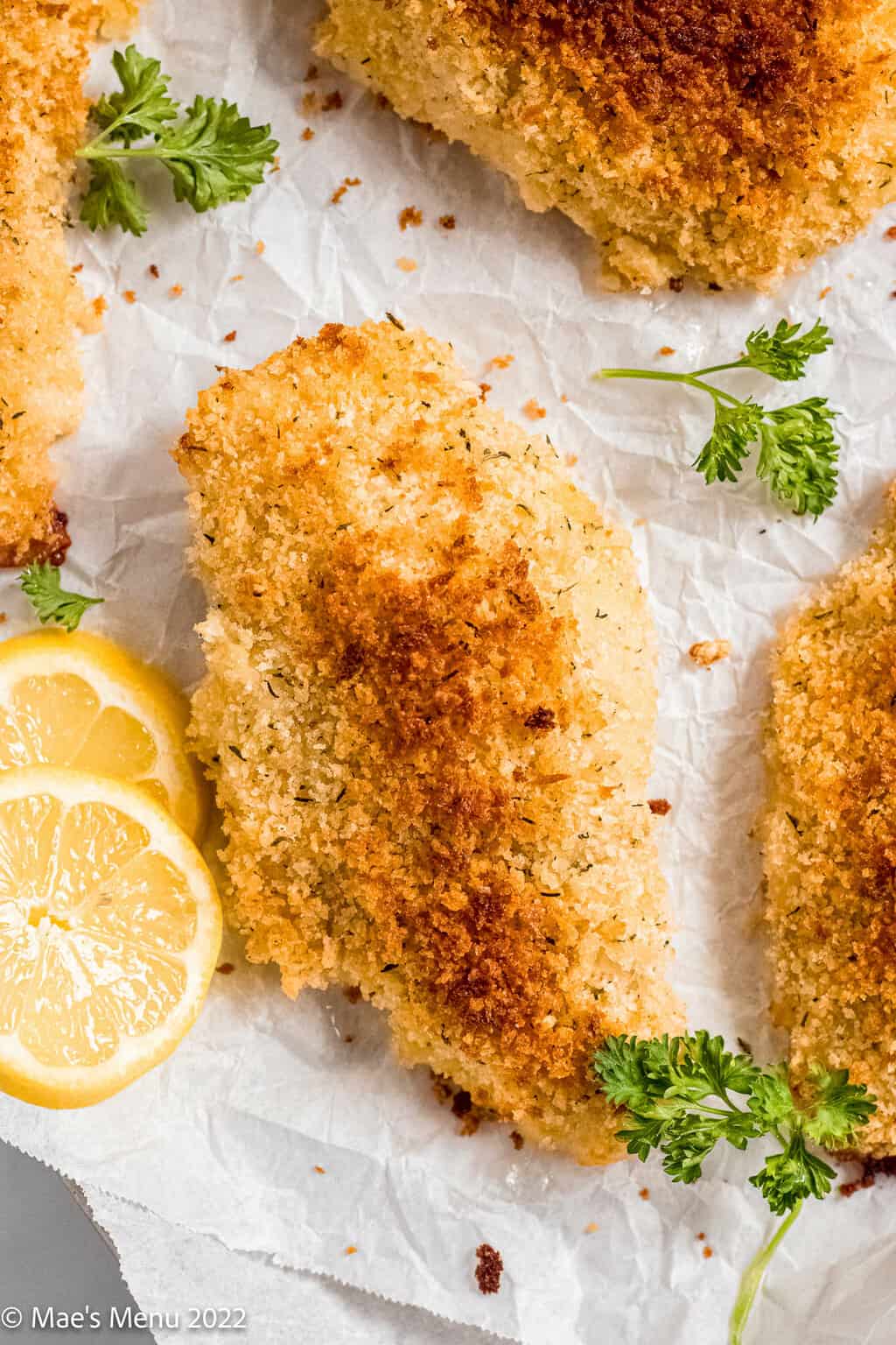 An up-close overhead shot of a panko crusted chicken breast on a baking sheet with parlsey and lemon.