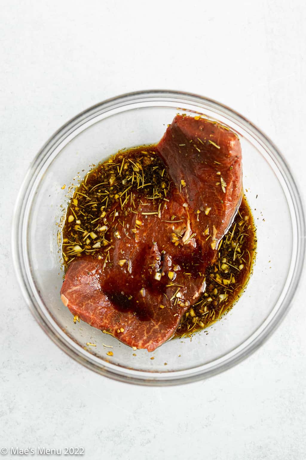 An overhead shot of a clear mixing bowl with flat iron steak in the marinade.