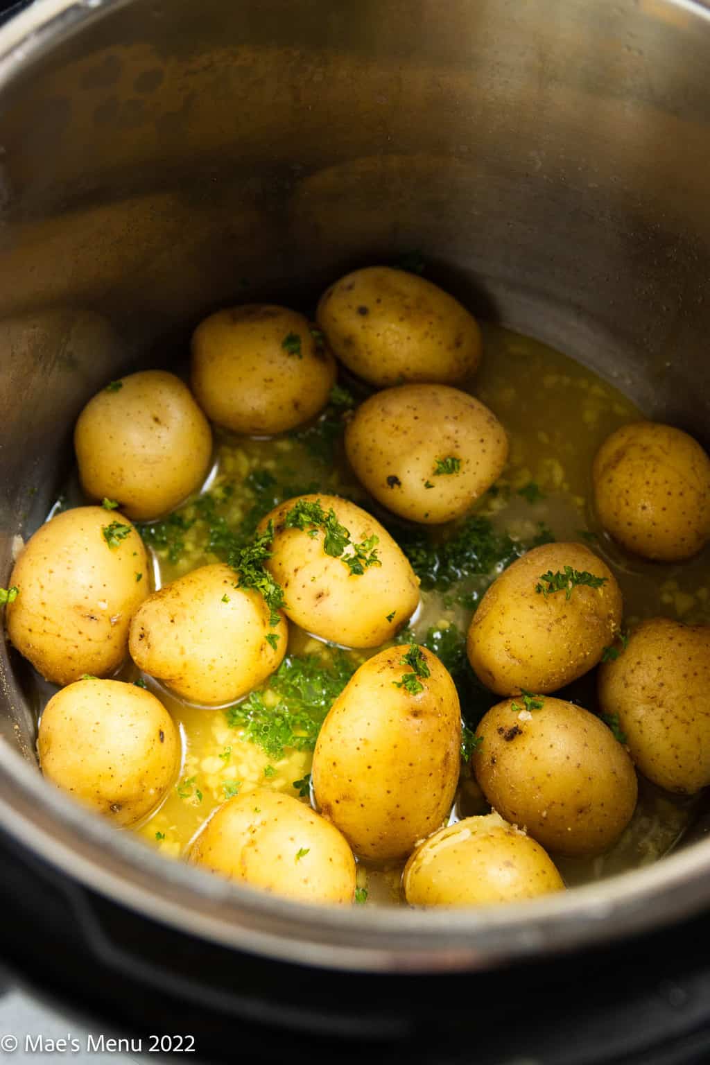 An instant pot with potatoes, garlic, olive oil, and parsley.