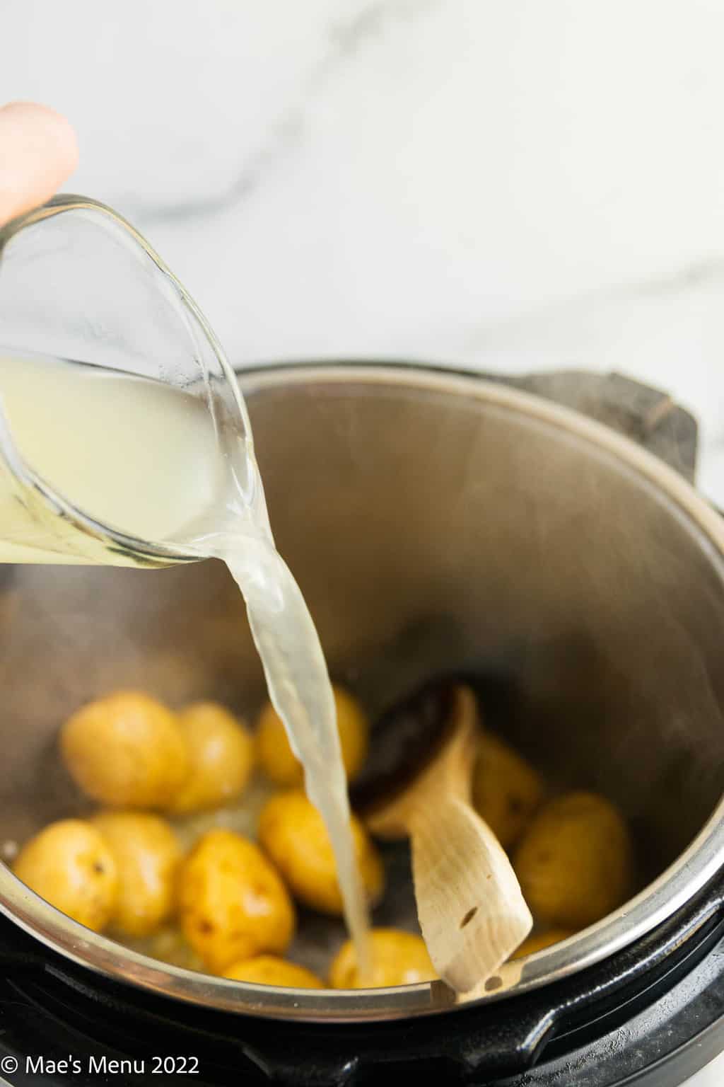 Pouring chicken broth into an Instant pot with potatoes.