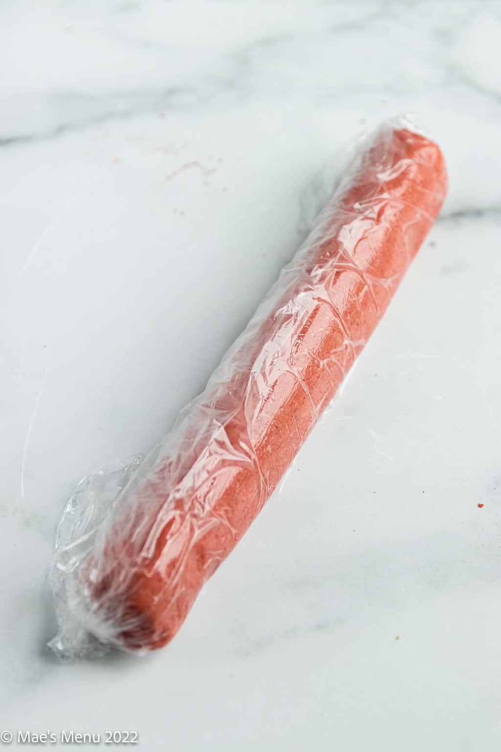 A cylinder of rolled strawberry shortbread in plastic wrap.