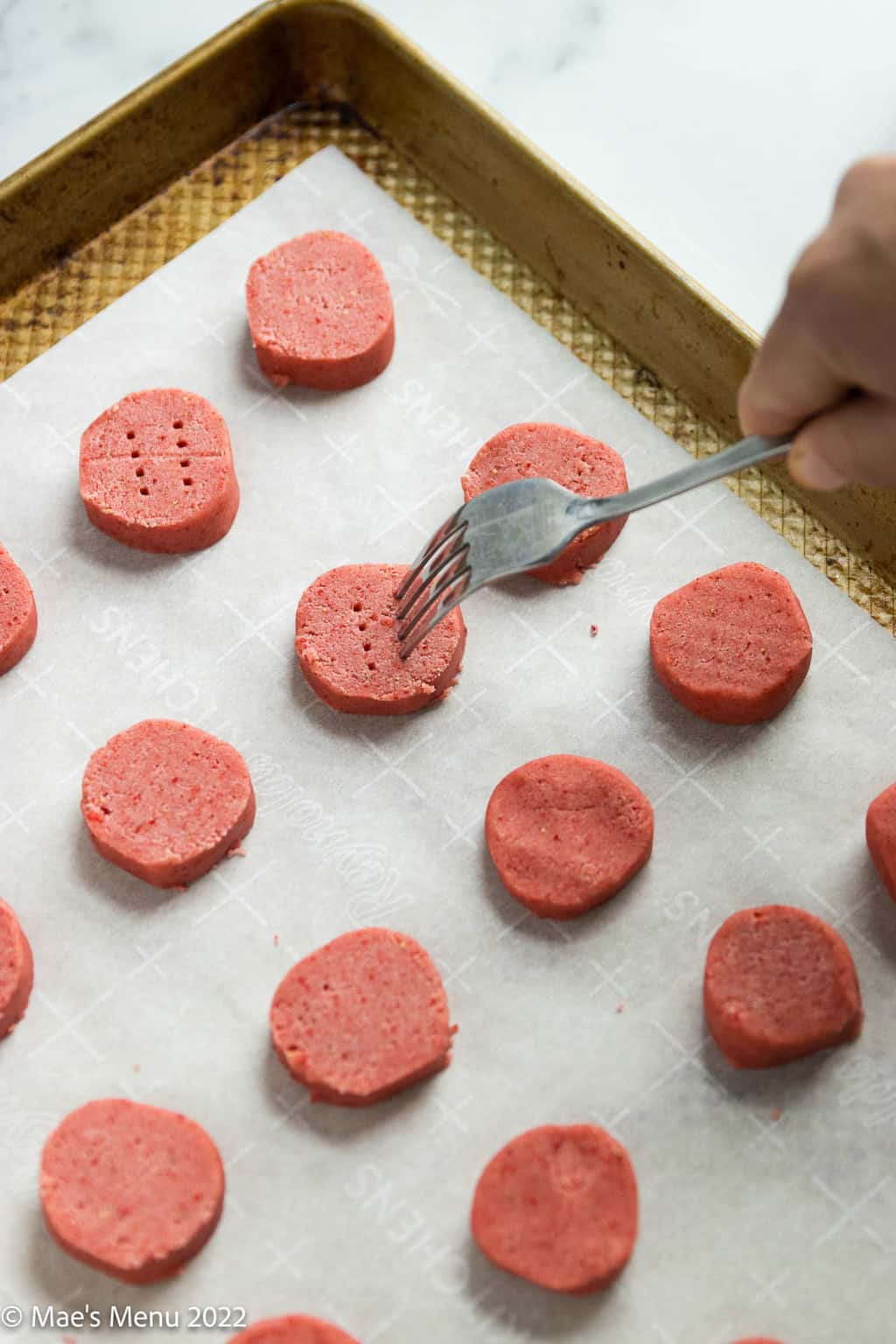 Poking holes in the top of the strawberry cookies with a fork.