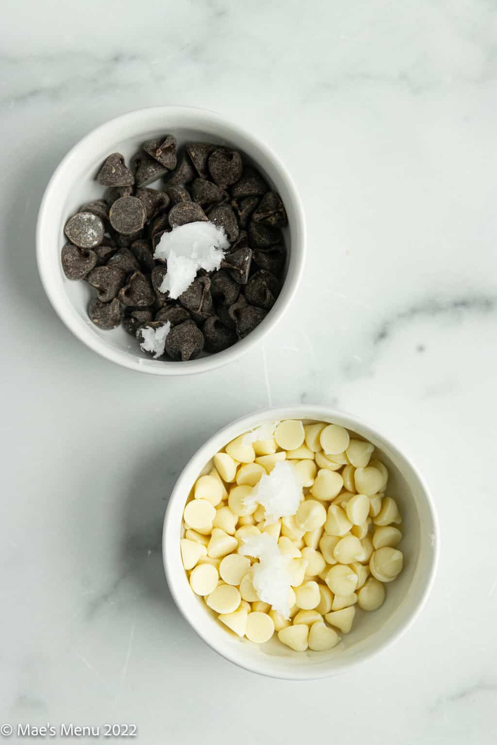 A small dish of chocolate chips and coconut oil and a small dish of white chocolate chips and coconut oil.