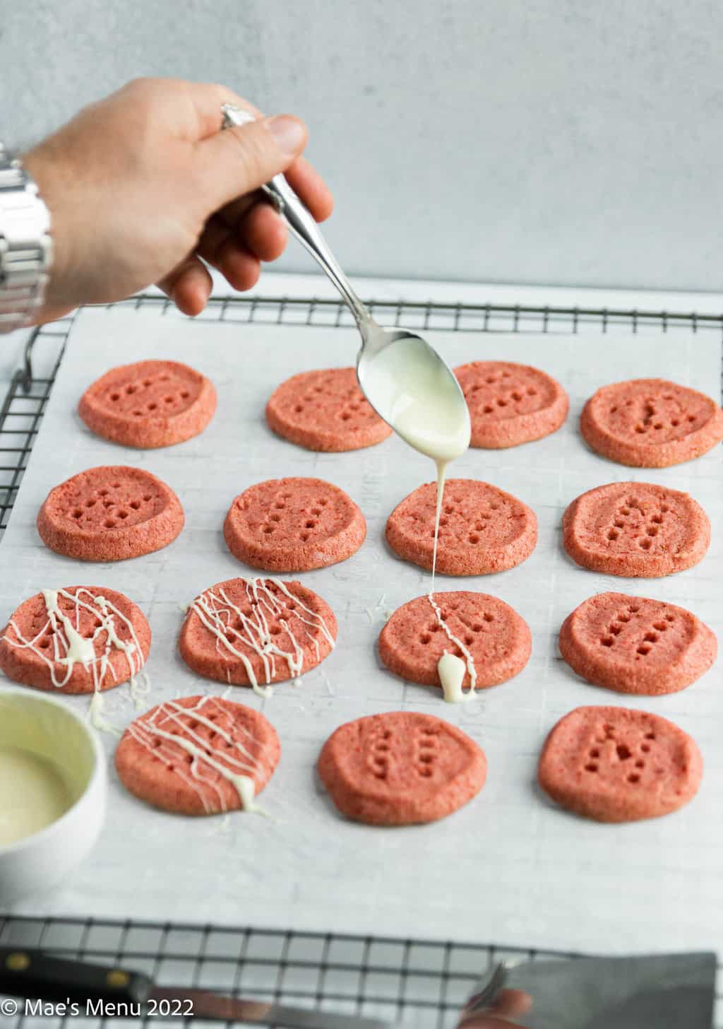 Drizzling melted white chocolate over the strawberry cookies.