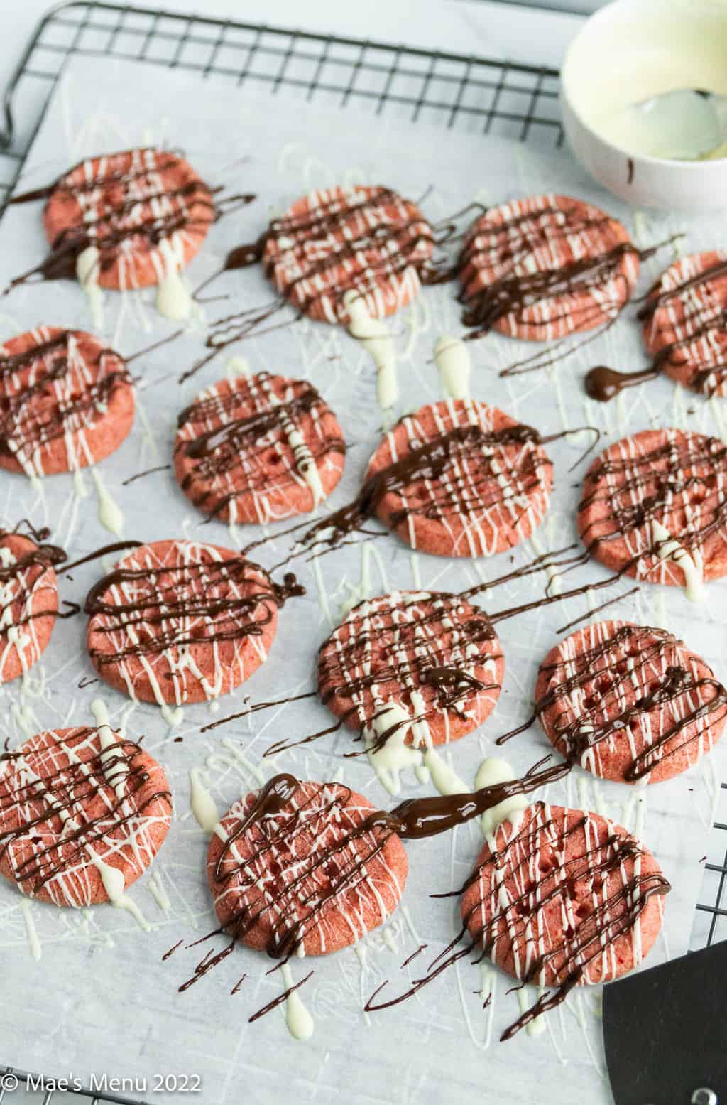 A cooling rack of strawberry cookies drizzled with white chocolate and chocolate.