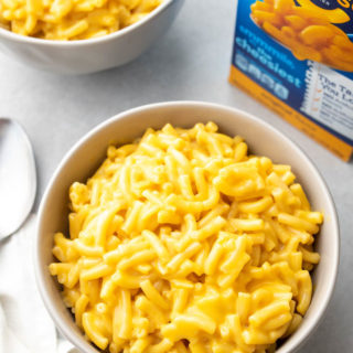 A large bowl of kraft mac and cheese in a white bowl with a box of the macaroni and cheese in the background.