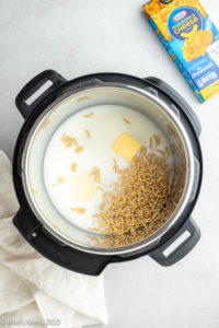 An overhead shot of an instant pot with macaroni, butter, water, and milk on a counter next to a box of the mac and cheese.