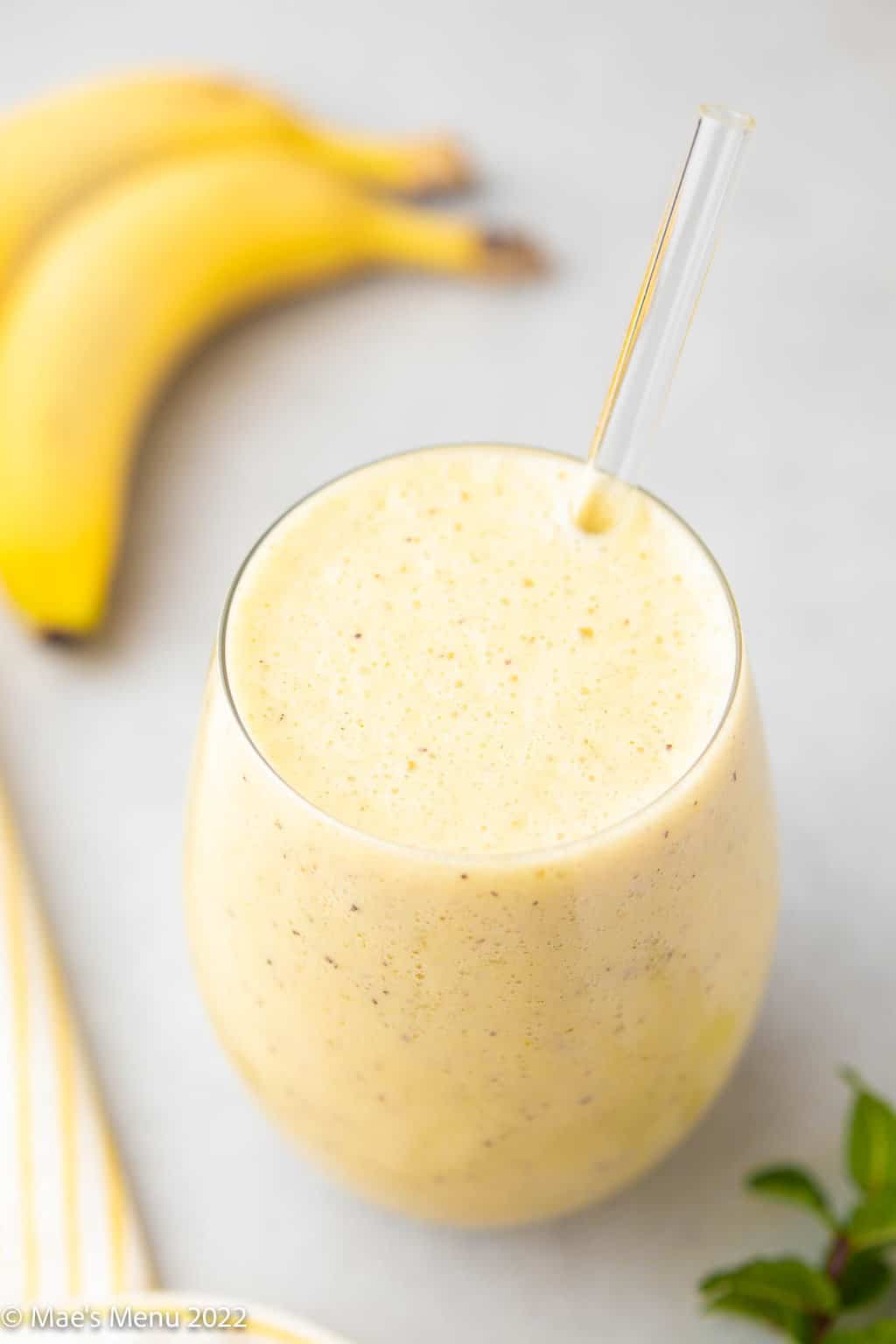 An up-close shot of a glass of pineapple banana smoothie with bananas in the background.