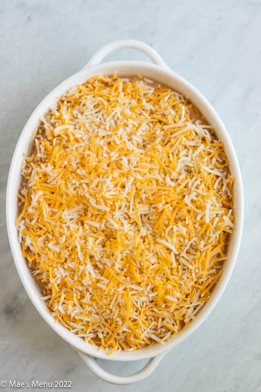 An overhead shot of a white pan of refried bean dip with shredded cheese.
