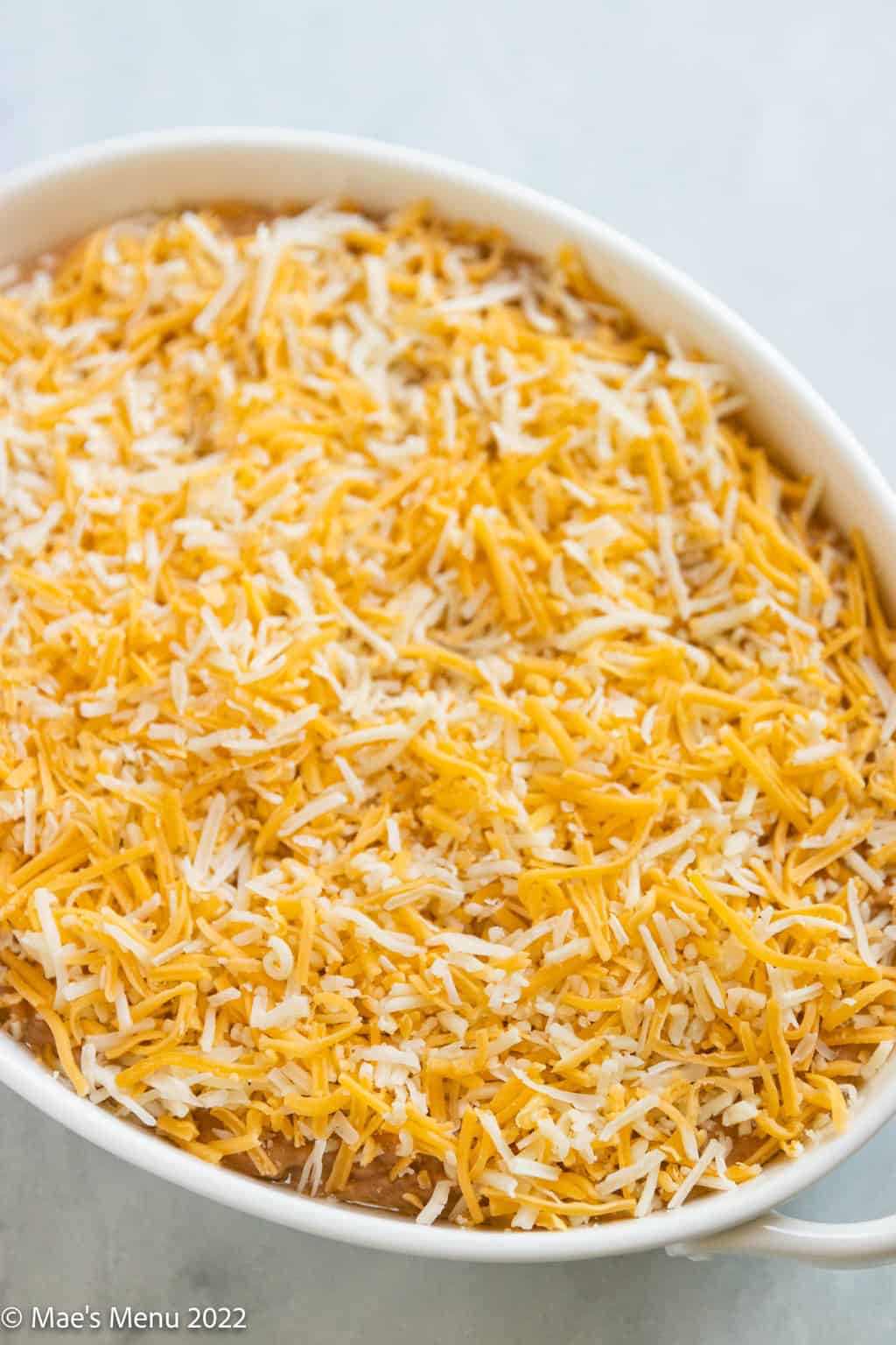 An up-close shot of a white dish of refried bean dip with shredded cheese.