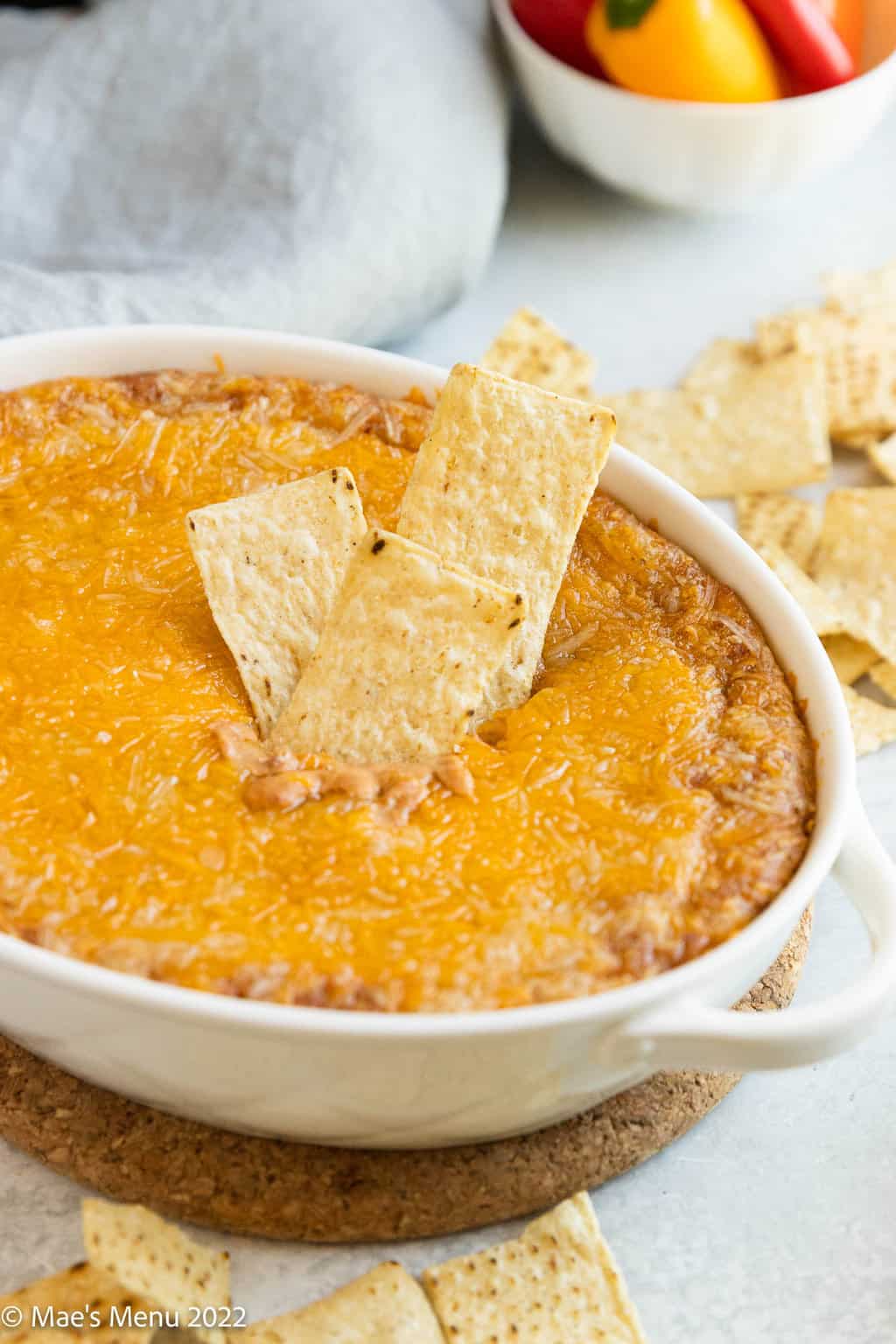 A white dish of cheesy refried bean dip with tortilla chips in it.