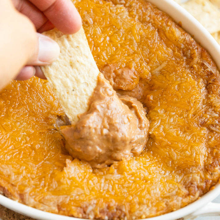 A hand dipping a dip into the refried bean dip with cream cheese.